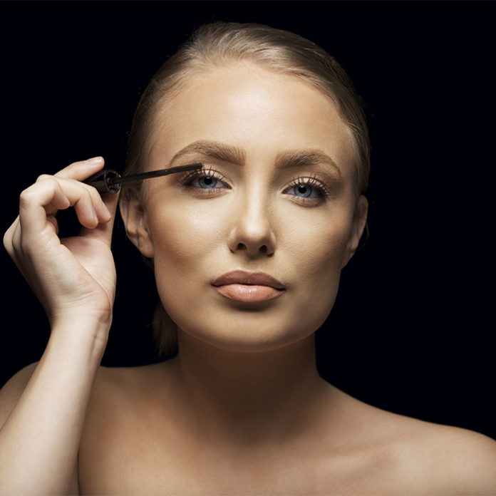 Attractive woman putting mascara on her eyelashes