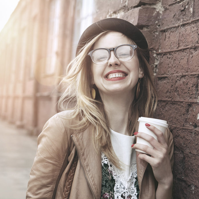 Cheerful woman in the street drinking morning coffee in sunshine light cheerful woman