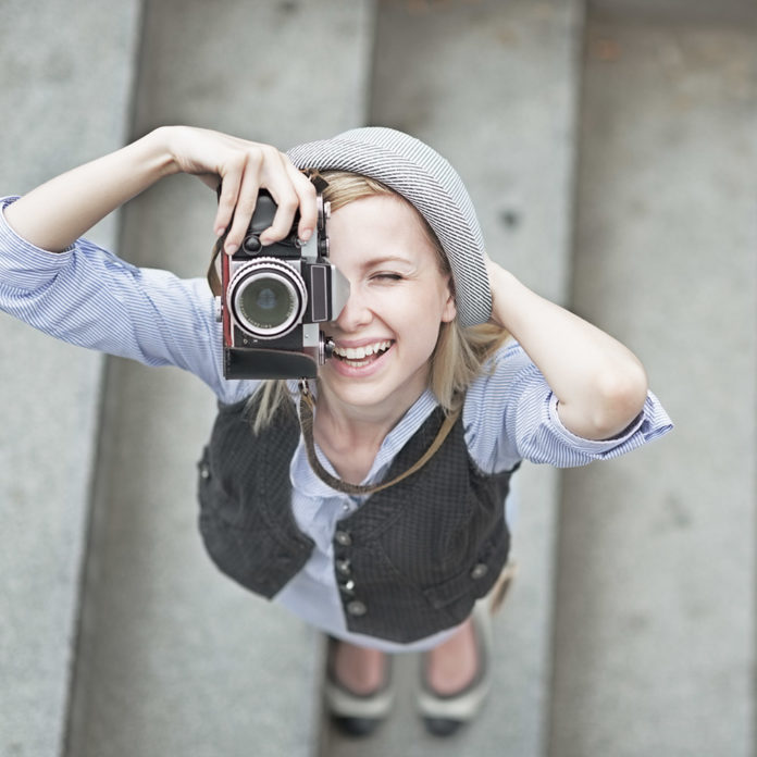 Happy hipster girl making photo with retro camera on city street creativity