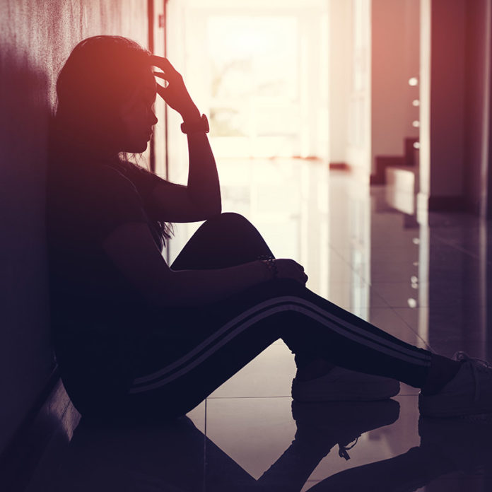 Silhouette of sad and depressed women sitting at walkway of condominium or office with backlit and lens flare,sad mood,feel tired, lonely and unhappy. restless